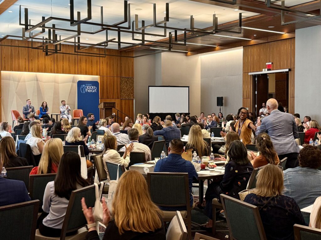 Audience seated at round tables watching a panel discussion at an Every 100th Heart event