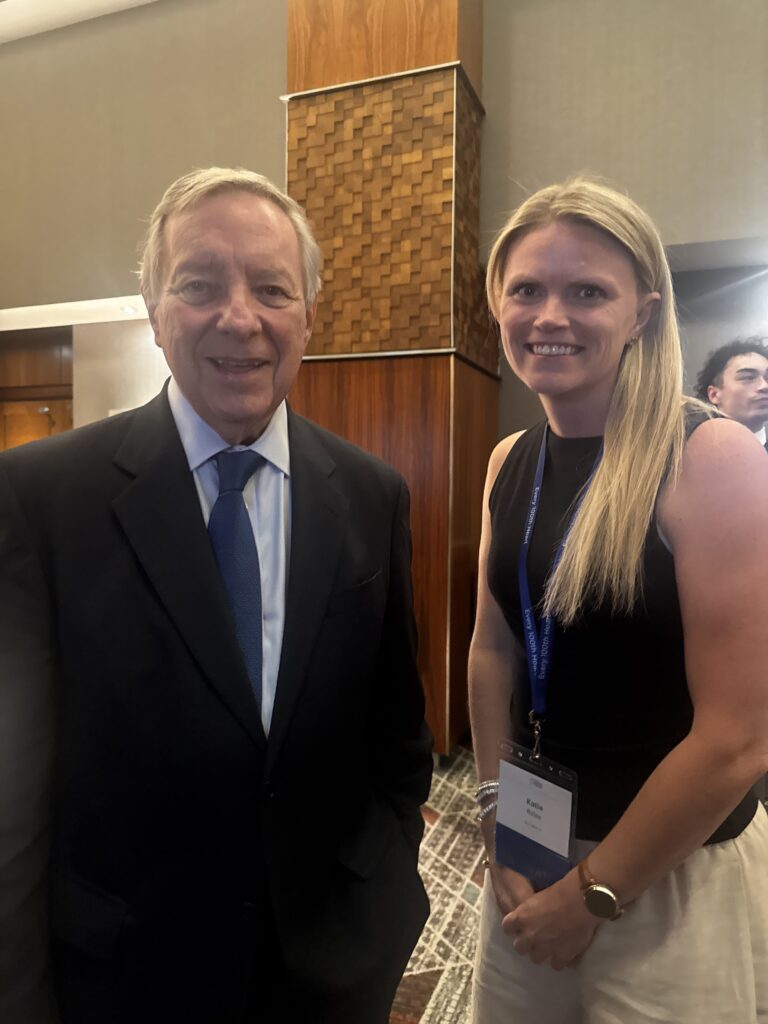 Woman wearing an event badge posing with a man in a suit at a conference